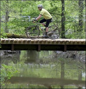 Blade reporter Mark Reiter rides over a bridge where about a dozen volunteers helped on Wednesday to put down planks on log rails to finalize the trail at Oak Openings Metropark.
