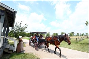 Employee Judy Dietrich waves to a group of visitors who are taking a horse and buggy tour of Sauder Village.