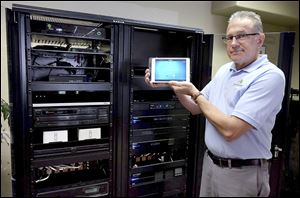 Kurt Hisey of Jamiesons’ Audio/​Video in Sylvania Township holds a touchpad that controls the whole-house remotely located distributed audio and video system, in background. 