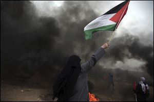 A woman waves a Palestinian flag in front of black smoke from burning tires during a protest at the Gaza Strip’s border with Israel.