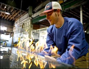 Desmond Alcock, a second generation apprentice, lights a part of a glass on fire pane to cut it down at Toledo Mirror and Glass in Toledo on Thursday. He's using the fire to get through the laminate layer in this particular pane of glass.